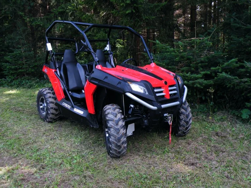 Red side-by-side off-road vehicle parked beside a wooded trail.