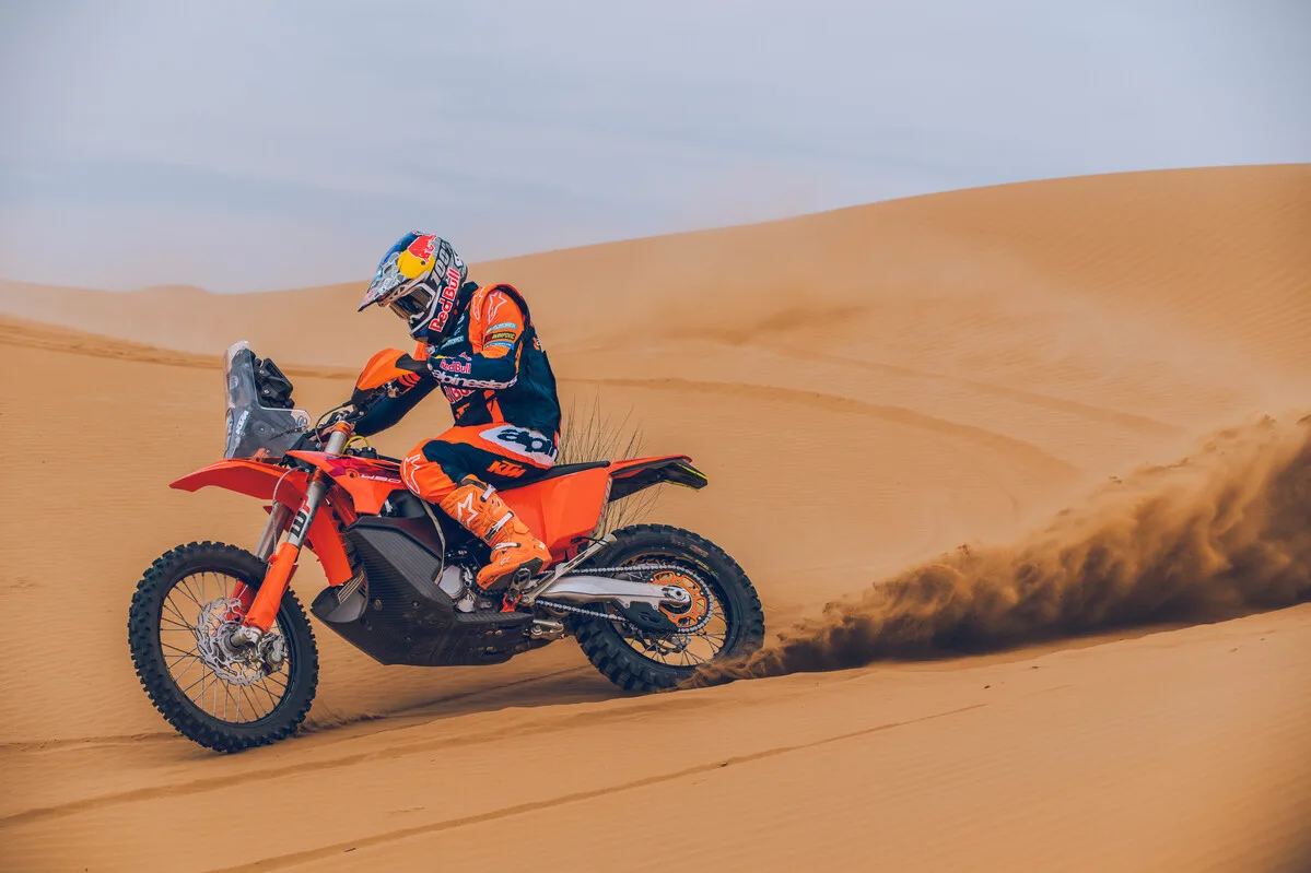 2027 KTM 450 RALLY REPLICA being ridden across desert dunes.