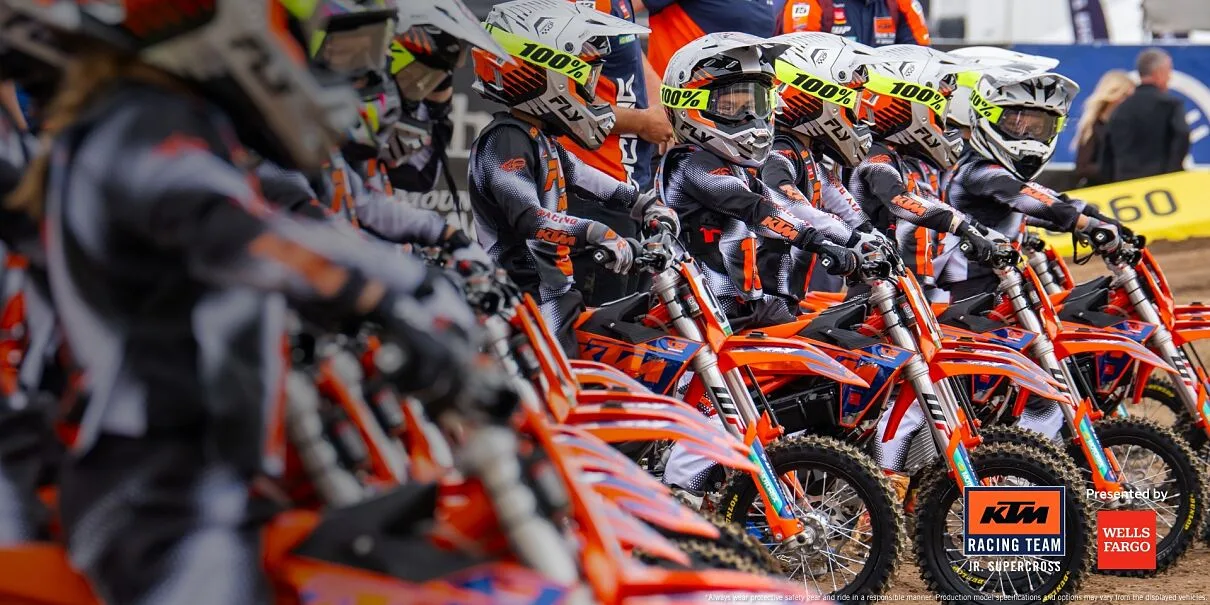 Young KTM Junior Supercross riders lined up on orange electric minibikes