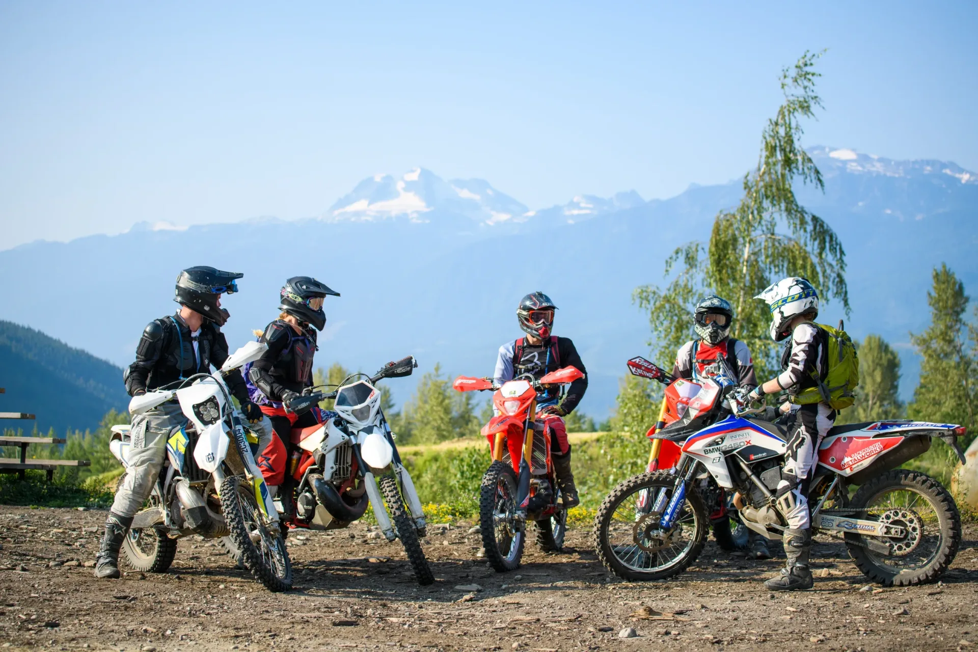 Revy Riders dirt bike riders gathered above Revelstoke with mountain scenery in the background