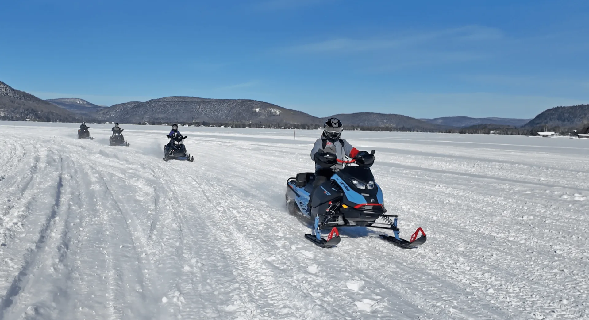 Snowmobilers cross an open snow-covered area in an FCMQ promotional photograph.