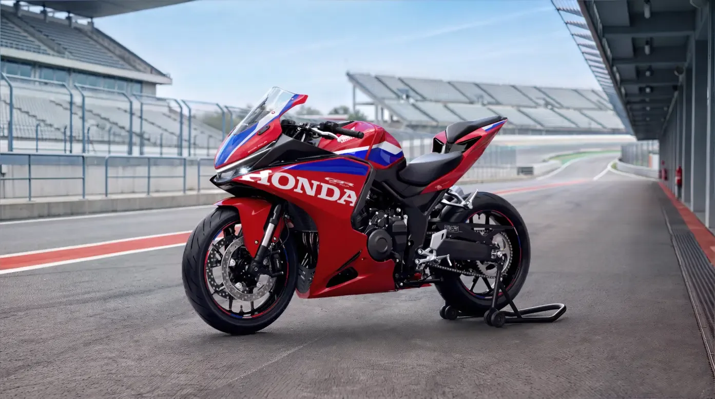 Red Honda CBR500R Four in a front three-quarter view on a paddock stand beside a circuit