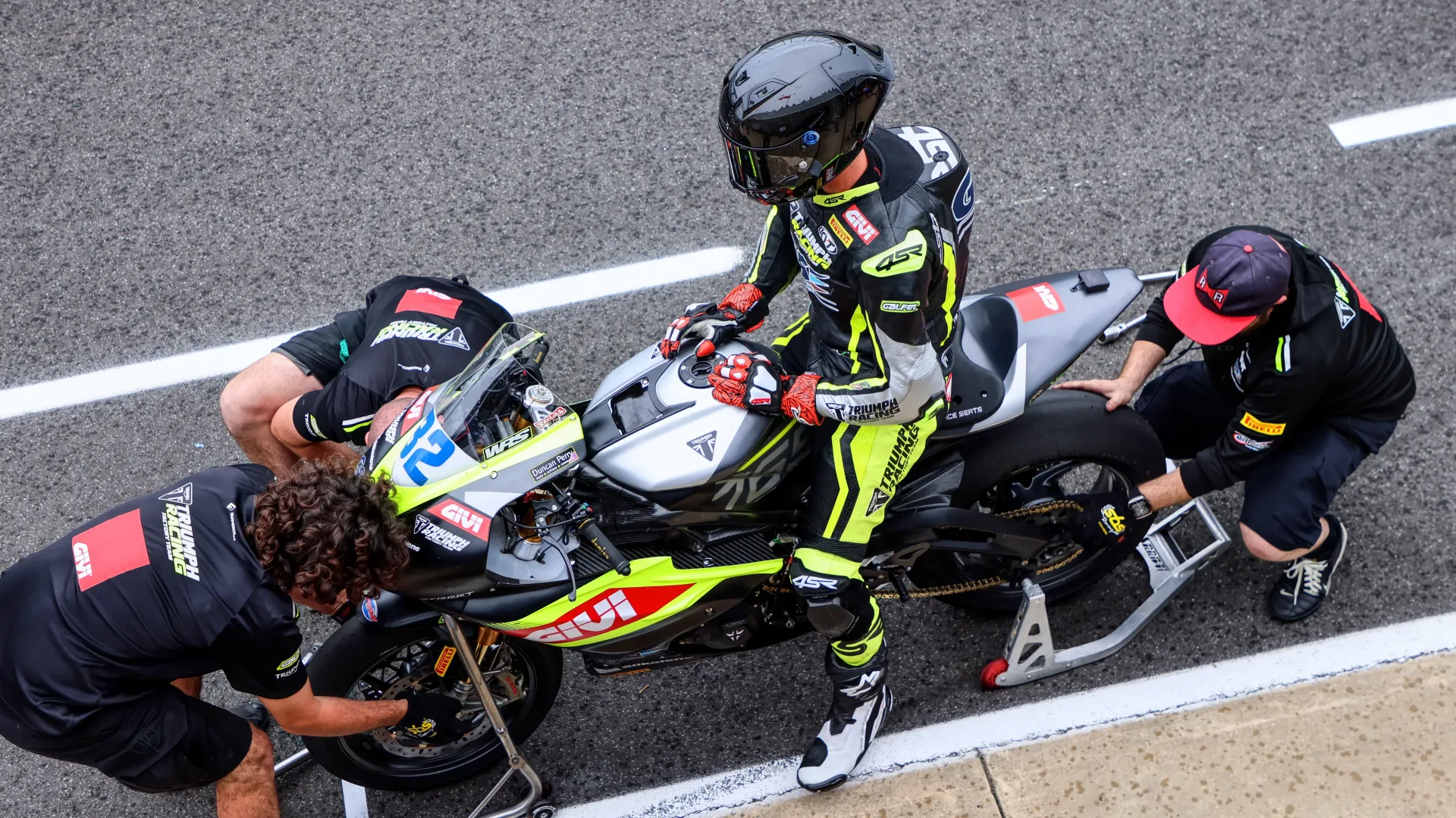 Oli Bayliss seated on a number 32 PTR Triumph race motorcycle with team members beside it