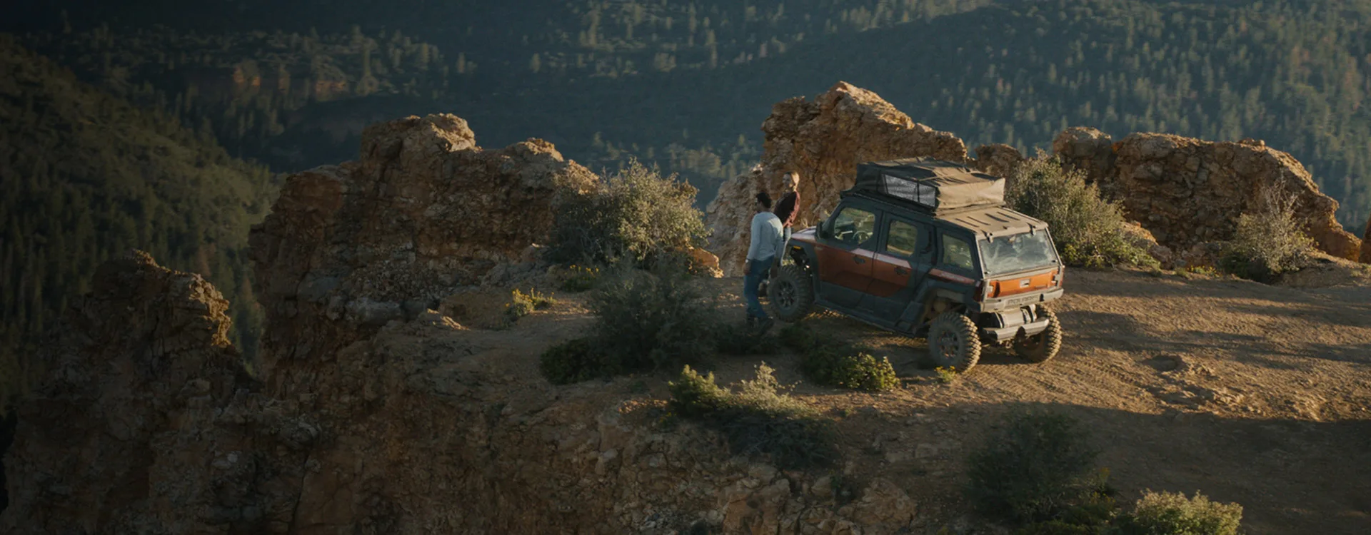 A Polaris XPEDITION side-by-side with camping equipment parked at a wooded mountain overlook.