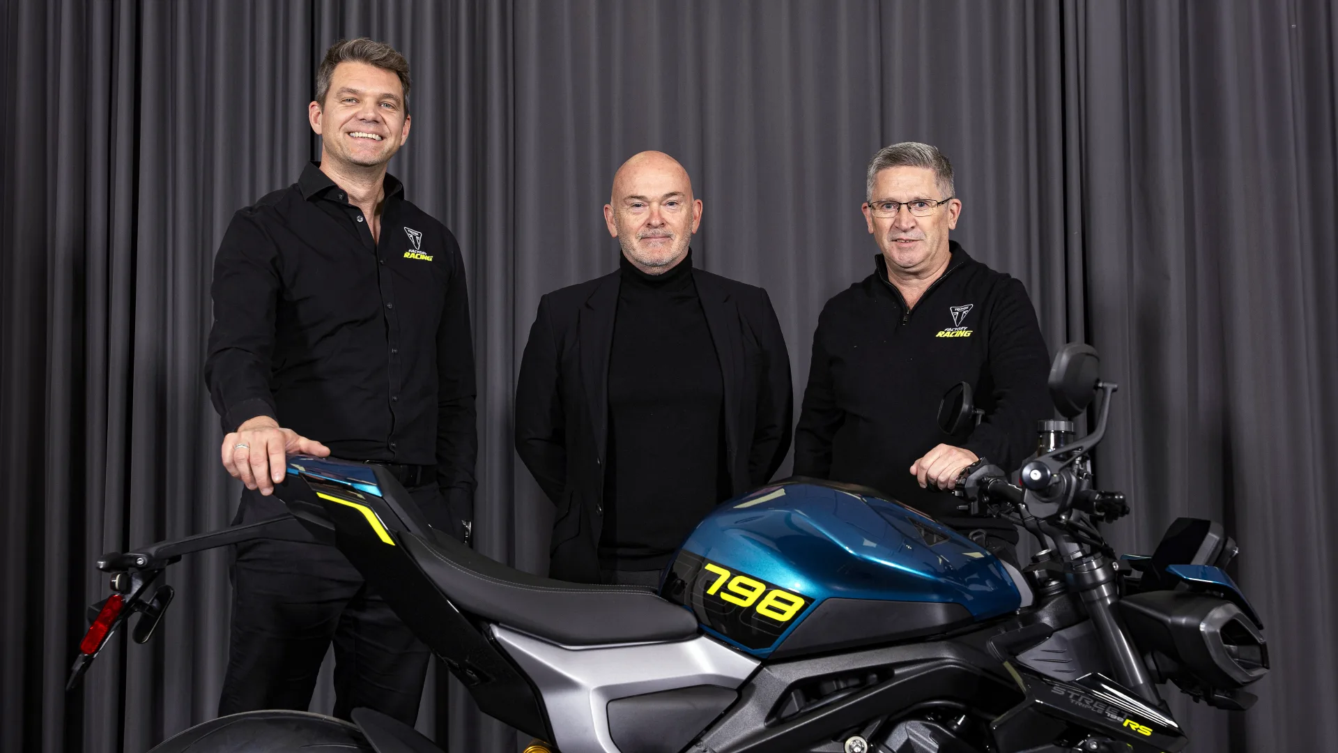 Ian Kimber, Mark Griffiths and Steve Sargent standing beside the Triumph partnership motorcycle